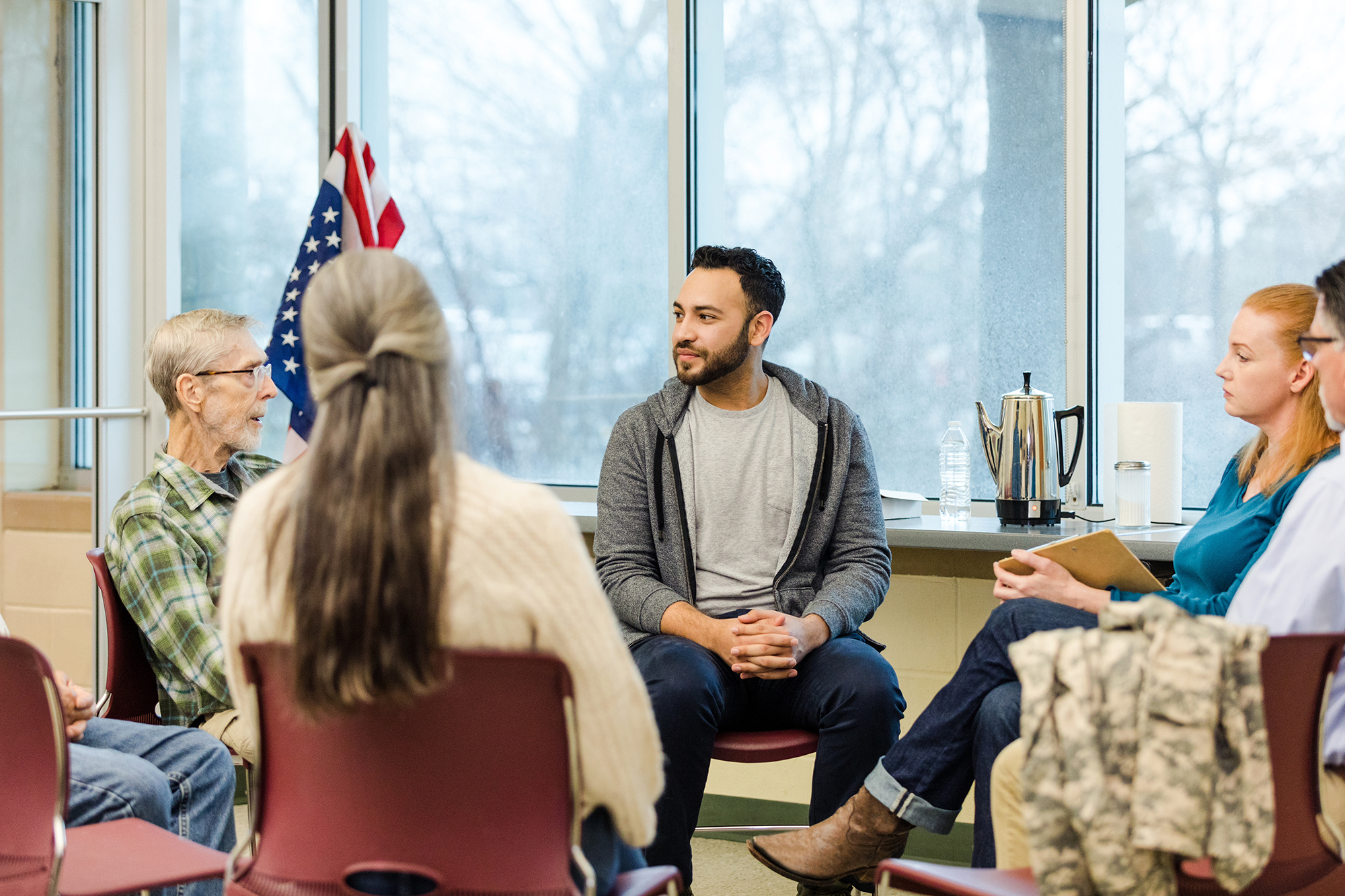 A multiracial, multigenerational group of military vets meet for group therapy on the Air Force base.